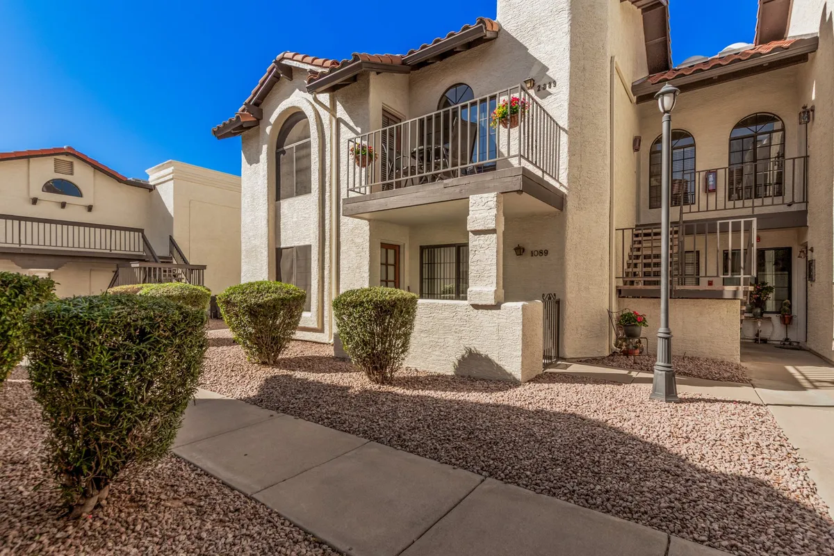 The photo features an exterior view with charming arched windows, a flower-adorned balcony, and a serene pathway leading to the entrance. The presence of outdoor spaces such as the balcony hints at private retreats and opportunities to relax after a day out.