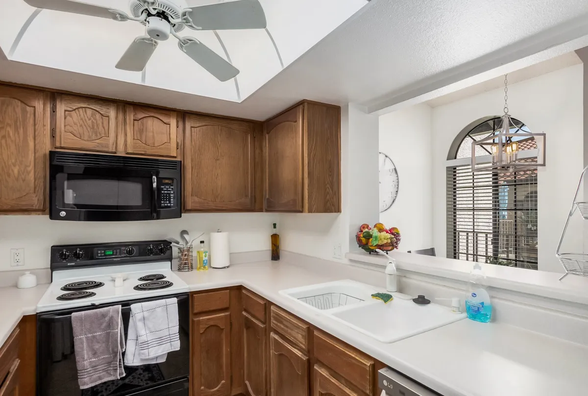 A bright and welcoming kitchen scene featuring modern cabinets, up-to-date appliances, a sink with a window view allowing natural light, and a fruit bowl on the counter. The ambiance suggests a warm, social atmosphere ideal for cooking, entertaining, and sharing meals.