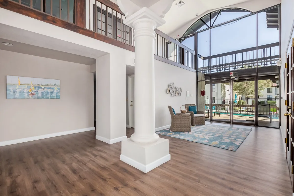 An inviting seating area bathed in sunlight from large glass windows, featuring stylish decor and a view of the pillar and wall art. The design creates a welcoming atmosphere for guests or residents alike.
