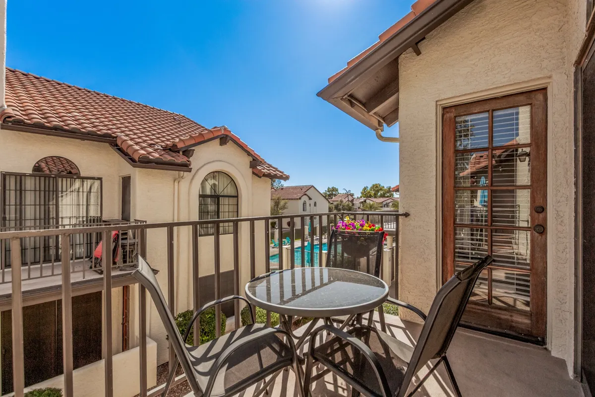 This image captures a private balcony with a table and chairs, set amid flower pots with colorful blooms. The balcony overlooks the community pool area, providing a peaceful spot to relax and take in the views, with a sense of privacy and serenity.