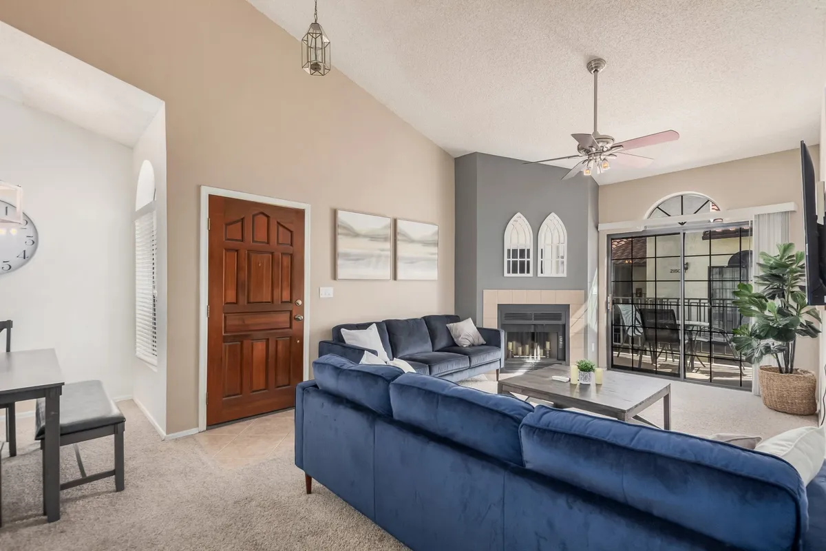 A stylish living area with a blue sectional sofa, inviting fireplace, arched windows, and a dining table set in the background. The large windows bathe the room in natural light and highlight the connection to the outdoors and communal areas.