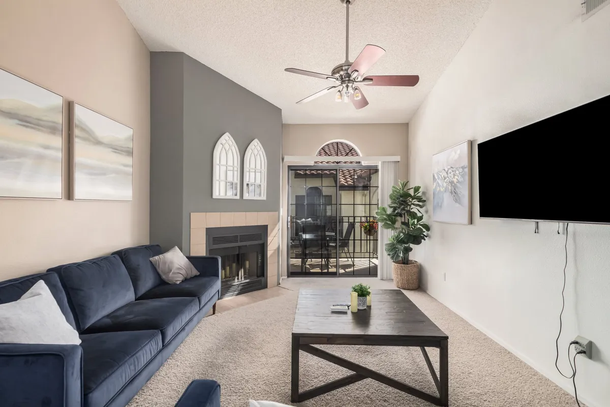 A cozy living area with a comfortable sofa, fireplace, coffee table, bright windows, and a leafy plant. The room is bathed in natural light, suggesting a warm, tranquil environment for both relaxation and entertaining.